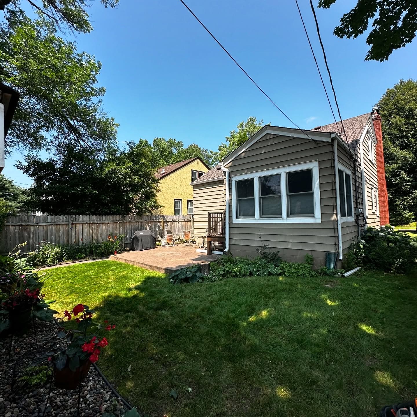 Backyard view featuring a quaint house, green lawn, and vibrant garden under a clear blue sky.