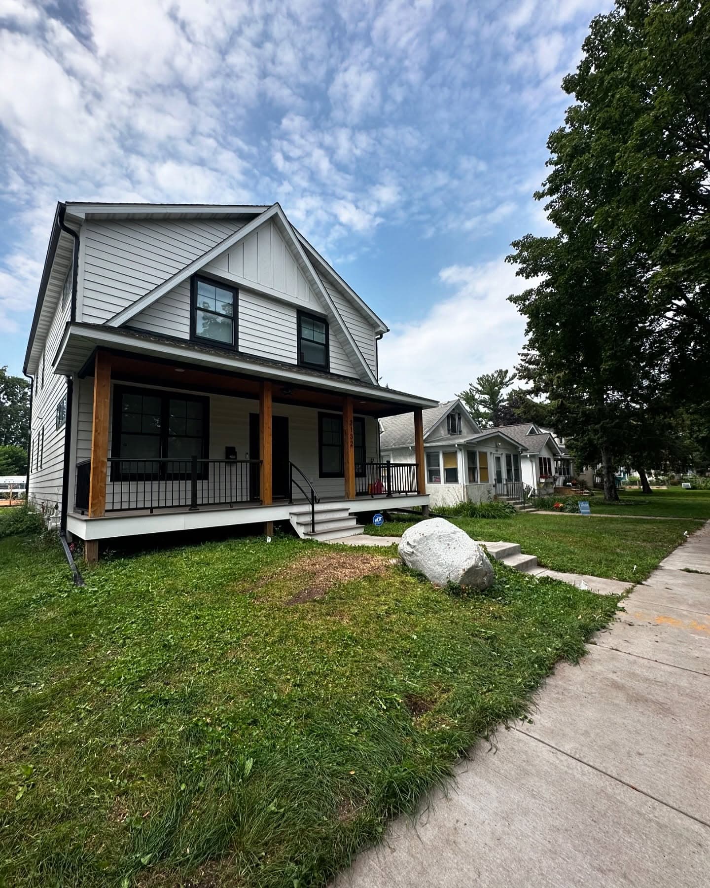 Modern two-story house with porch, vibrant lawn, and nearby trees. Ideal for family living.