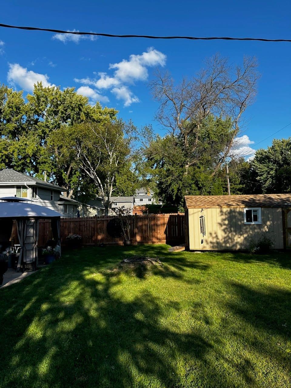 Spacious backyard with green grass, trees, and a garden shed under a blue sky.