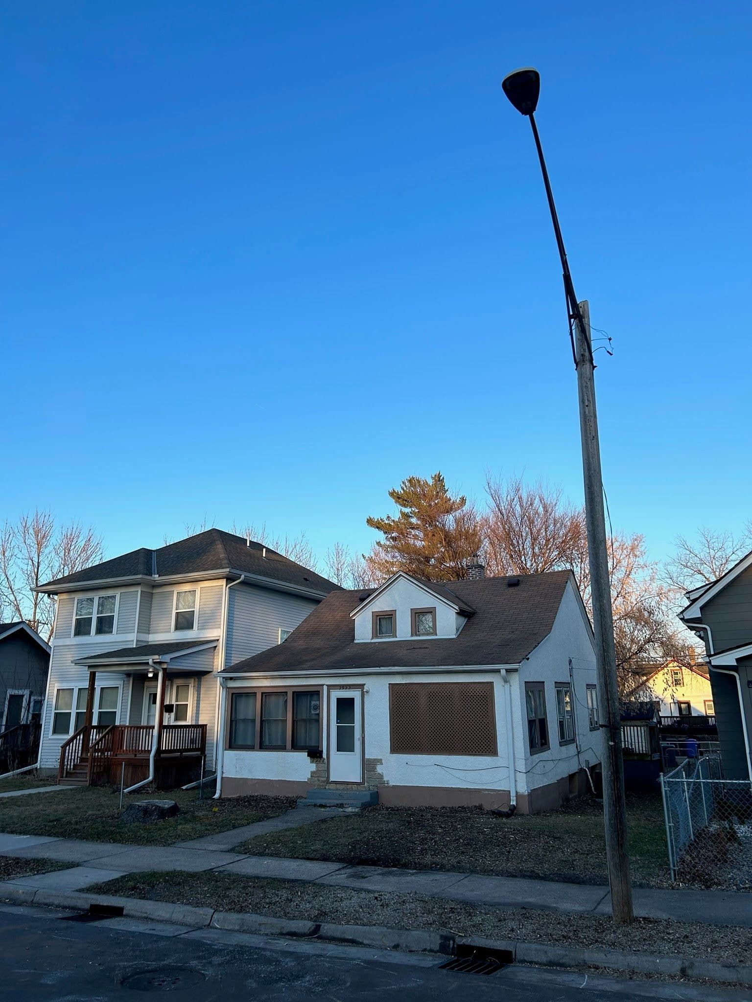 Abandoned white house with boarded windows and a streetlight in a residential neighborhood.